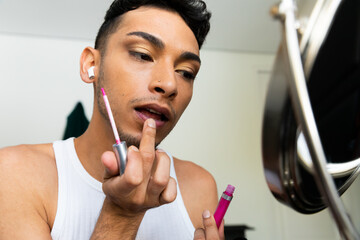Biracial transgender man looking in mirror and putting on make-up, applying lipstick