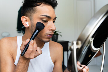 Biracial transgender man looking in mirror and putting on make-up, applying blush - obrazy, fototapety, plakaty