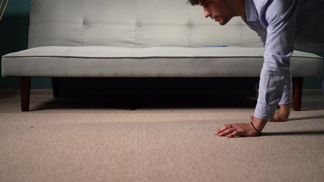Handsome guy looking for a lost wallet under the sofa