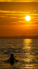 Silhouette of a girl in the water during a virant orange sunset in the sea, in Ao Nang, Thailand