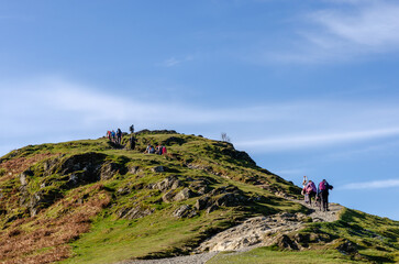 Group of people hiking to the top of a mountain on a natural pathway in Lake District, England, UK