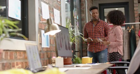 Happy diverse male and female designer brainstorming at glass wall in fashion studio, in slow motion - Powered by Adobe