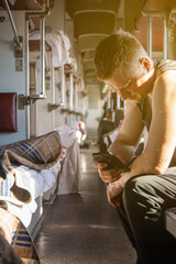 a man using a phone in the aisle of a second-class carriage of a high-speed train waiting for his stop, the background is blurred