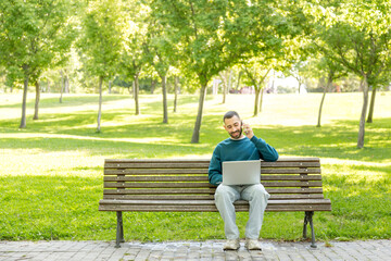 Young student multitasking with laptop and phone on park bench