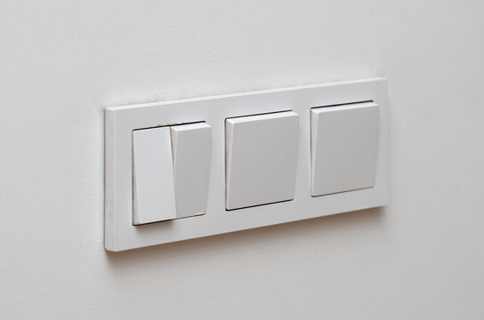 Block of three white plastic electrical switches on a white wall