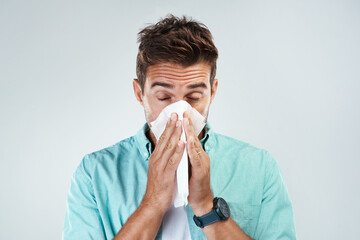 Sick, tissue and face of man blowing nose in studio with flu, illness and virus on white...