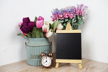 Empty easel chalkboard sign mockup with alarm clock and flower decoration