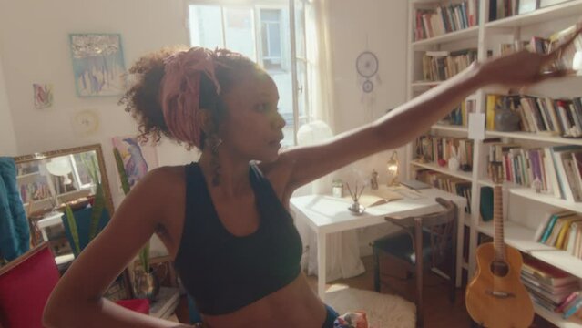 Young attractive black girl wearing pareo and bra dancing sensually in the living room filled with sunlight. Handheld shot, lens flare