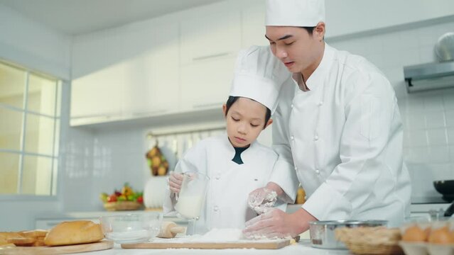 Asian chef man and boy in chef uniform cooking or baking together in kitchen room. Chef teaching little boy cooking or baking at freetime or holiday