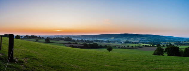 Fototapeta premium An early morning with a sky full of beautiful colors during sunrise in the rolling hills landscape of Limburg with spectacular views over the typical small villages of this region