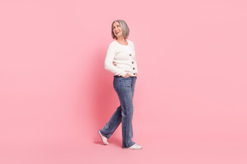 Naklejka premium Full size profile photo of positive lovely aged lady put hands pockets walk look behind empty space isolated on pink color background