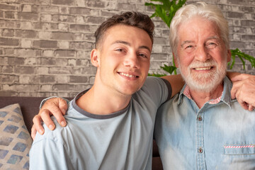 Portrait of family couple, a young boy and his old grandfather smiling looking at camera while sitting on the sofa at home, old and new generation - caring for the people we love