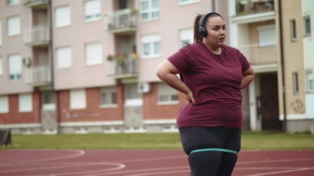 Exhausted Caucasian overweight woman standing on basketball court breathing in and out. Portrait of a tired young obese woman resting after a morning workout outdoors.