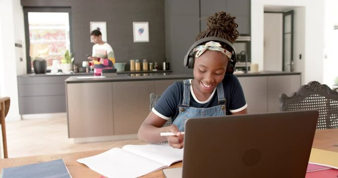 Happy african american girl in online class using headphones and laptop in slow motion