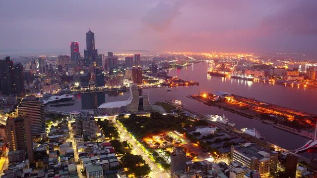 Aerial hyperlapse of Kaohsiung, a vibrant seaport city in Southern Taiwan, with 85 SKy Tower standing out in downtown next to the harbor and city lights begining to glow at nigthfall in rush hour