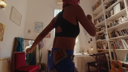 Young relaxed African-American girl dancing barefoot and enjoying the music, spending the day at home. Zoom shot, full length