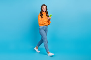 Full length photo of shiny pretty lady dressed orange pullover writing sms twitter telegram facebook isolated blue color background