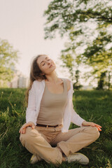 Obraz premium Yoga at park with sunlight. Young woman in lotus pose sitting on green grass. Concept of calm and meditation.
