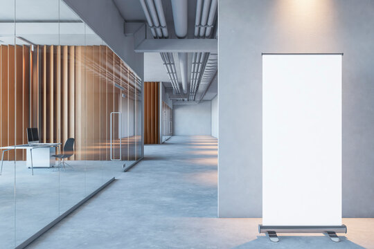 Front view on blank white rollup poster with space for logo or text on grey partition background on concrete floor in spacious office with wooden walls and glass doors. 3D rendering, mockup