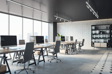 Open office interior with desks, computers, a concrete floor, and black ceiling. A window provides natural light. Modern workspace design and business background. 3D Rendering