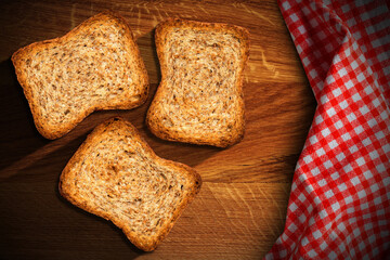 Close-up of three rusks on an old wooden table with a red and white checkered tablecloth.