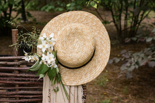 A beautiful straw hat with a bouquet of white flowers hangs on the fence. Nature and garden summer background.