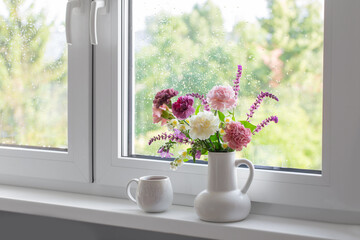 pink, purple and white  flowers in white jug with cup of tea  on windowsill