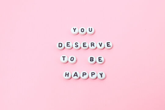Top view of "you deserve to be happy" quotes made out of beads on pink background. motivation and success concept