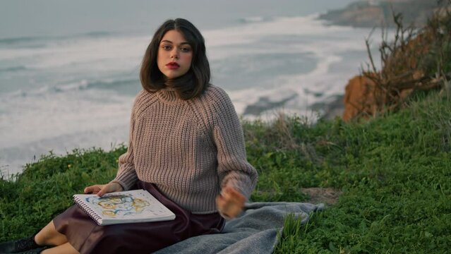 Dreamy woman relaxing blanket with book looking evening ocean. Model posing.