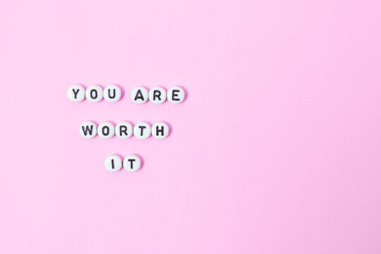 Top view of "you are worth it" quotes made out of beads on pastel background. motivation and success concept
