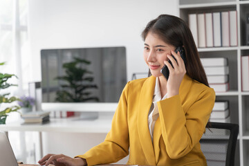 Businesswoman talking on cellphone holding paper sitting at desk and using laptop computer working online in office. Entrepreneurship and business career, distance freelance job concept.