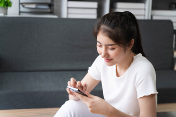 Young woman of Asian use mobile cell phone stay at home rest relax spend free spare time in living room indoor.Female feeling joy enjoying with mobile phone.