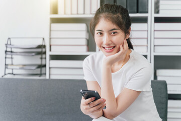 Young woman of Asian use mobile cell phone stay at home rest relax spend free spare time in living room indoor.Female feeling joy enjoying with mobile phone.