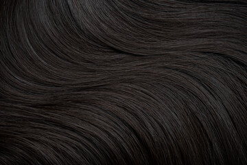 Brunette or black hair. Female long dark hair in black. Beautifully laid curls. Closeup texture in a dark key. Hairdressing, hair care and coloring. Shading gray hair. Background with copy space.