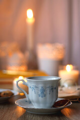 Cup of tea or coffee, plate of cookies, books, e-reader, pencil and lit candles on the table. Selective focus.