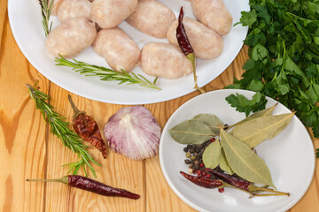 Raw thick short sausages among spices and greens, top view
