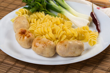 Serving of baked thick short sausages with pasta and greens