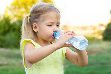 little child girl in yellow dress drinking water from bottle with closed eyes in nature in summertime