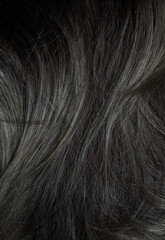 Brunette or black hair. Female long dark hair in black. Beautifully laid curls. Closeup texture in a dark key. Hairdressing, hair care and coloring. Shading gray hair. Background with copy space.