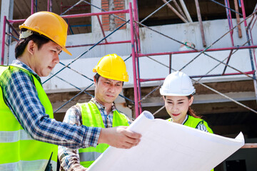 Architects, engineers and contractors holding construction drawings outdoor meeting in construction site. Industrial concept