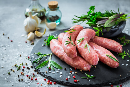 Raw sausages on slate, with herbs and spices, prepared for grill and BBQ