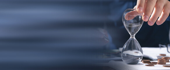 Businessman holding hourglass. Coins and business objects on the desk