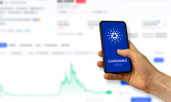 Hand holding a smartphone with a blue screen cardano. Ada crypto currency illustration on a trading chart background .