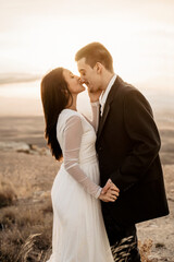 Pareja joven de novios recien casados celebrando su boda informal con una sesion de fotos al atardecer en el campo, ella le da un beso en la nariz