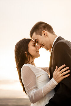 Pareja joven de novios recien casados celebrando su boda informal con una sesion de fotos al atardecer en el campo, se muestran su amor apoyando sus frentes como muestra de cari&ntilde;o