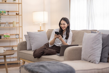 Obraz premium Portrait of a young happy asian female freelancer sitting on the couch and working on project, watching movie on phone laptop, studying, blogging, resting and chatting online.