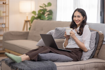 Portrait of a young happy asian female freelancer sitting on the couch and working on project, watching movie on laptop, studying, blogging, resting and chatting online.