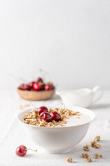 Bowl of homemade granola with nuts and cherry in white bowl on light background. Quick healthy breakfast