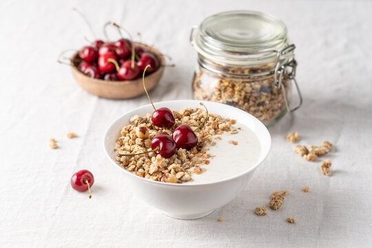 Bowl of homemade granola with nuts and cherry in white bowl on light background. Quick healthy breakfast