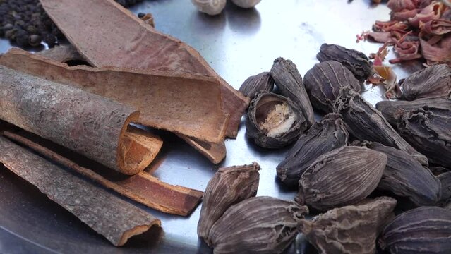 A close up shot of dried whole Indian spices on a big metal bowl.